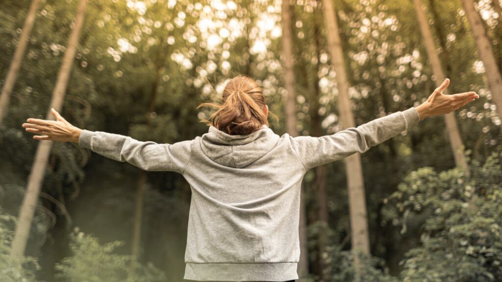 Woman raises her hands in sunny forest.